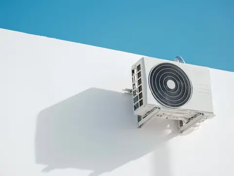 An air conditioning unit fixed to a white wall under a blue sky