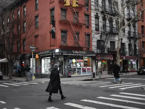 People crossing at an intersection in Brooklyn in front of a corner shop under brick apartment buildings