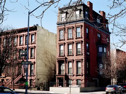 A row of brownstone houses on a Brooklyn street corner under a blue sky