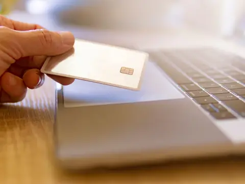 A hand holding a payment card over the keyboard of a laptop