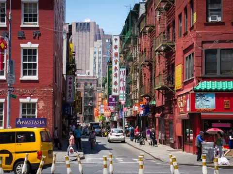 A street in Chinatown, New York, with red brick buildings, shop signs and a yellow taxi