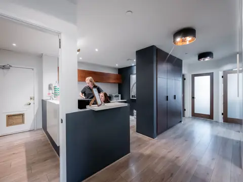 A clinic reception desk with two staff at a screen, and a corridor with wood floors and frosted doors