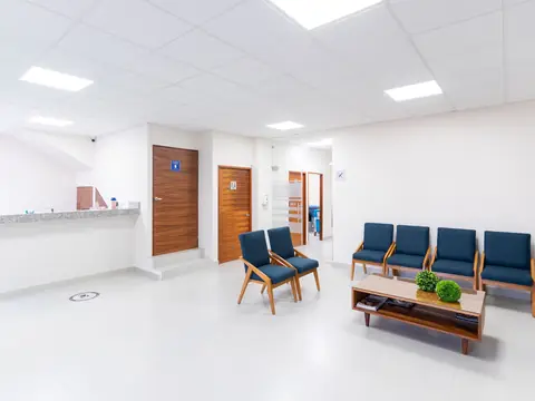 A bright clinic waiting room with blue chairs, a low table and a reception counter
