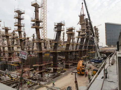 A large building site with rows of concrete columns in scaffolding, cranes and workers below