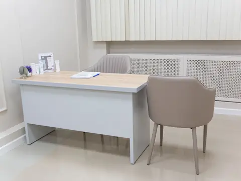 A consulting room desk with two grey chairs in front of a white wall