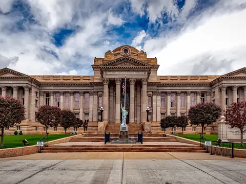 A wide stone courthouse with columns and steps behind a lawn, under a cloudy sky