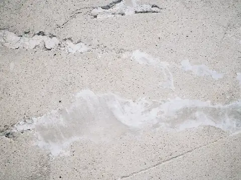 A pale concrete surface with a crack and patches of rough repair, seen from above