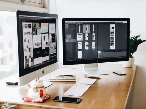 Two desktop screens on a wooden desk showing grids of page layouts