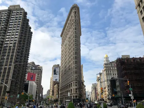The Flatiron Building in Manhattan seen from the street, with traffic, trees and taller buildings on both sides