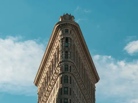 The top floors of the Flatiron Building in New York from below, against a blue sky with white clouds