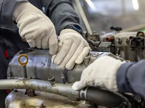Gloved hands loosening a bolt on an engine with a socket wrench