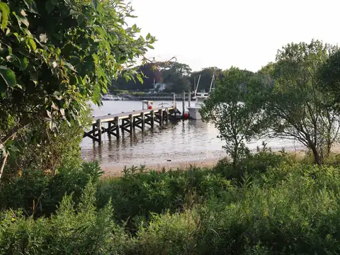 A wooden pier in calm water seen through green shrubs and trees at Hampton Bays