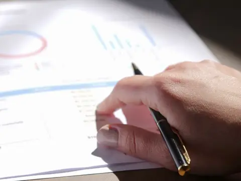 A hand holding a pen over a printed report with a ring chart and bar charts