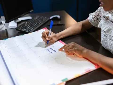 A hand writing with a blue pen in a large month-to-a-page desk calendar