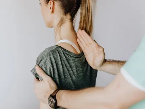 A practitioner's hands on the shoulder and back of a patient seen from behind