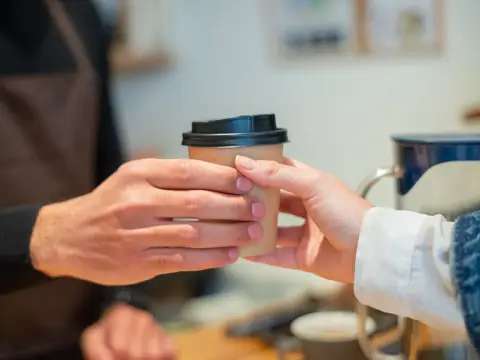 One hand passing a paper coffee cup to another across a counter