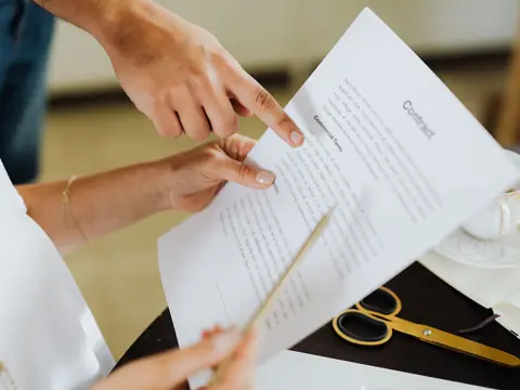 Hands pointing with a pencil at a line of a printed contract