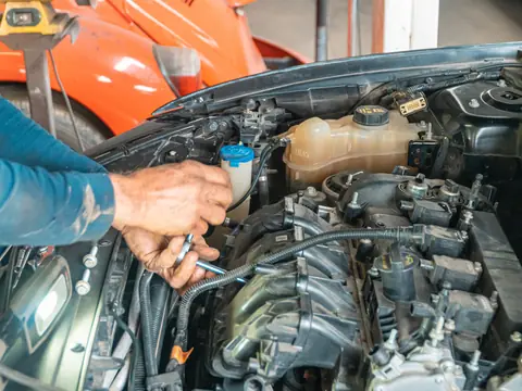 Two hands working inside the engine bay of a car