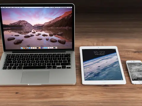 A laptop, a tablet and a phone side by side on a wooden desk