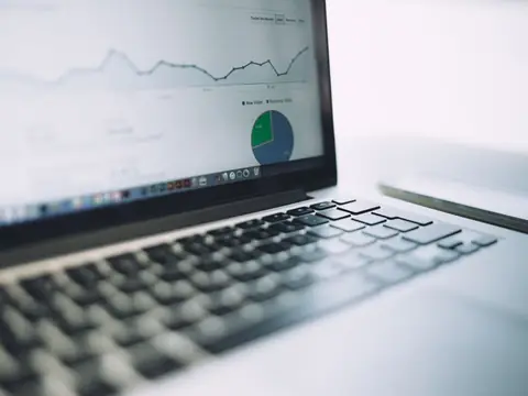A laptop screen showing a line chart of visits and a pie chart, with a phone lying beside the keyboard