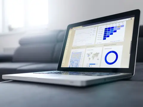 A laptop on a grey sofa showing a dashboard of bar charts, a map and a ring chart