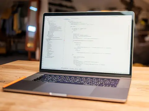 An open laptop on a wooden desk with a code editor on its screen