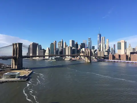 The Brooklyn Bridge and the Lower Manhattan skyline across the East River under a blue sky