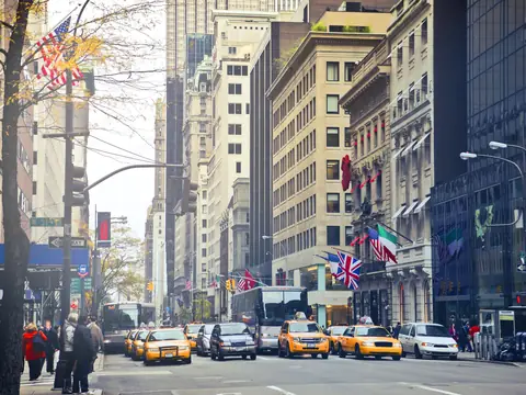 A Manhattan avenue with yellow taxis at a light and flags on the buildings