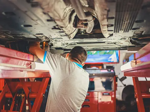 A mechanic seen from behind working under a car raised on a lift in a repair shop