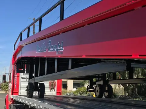 A red steel loading ramp on wheels with the name Medlin Ramps on its side, seen from below against a blue sky
