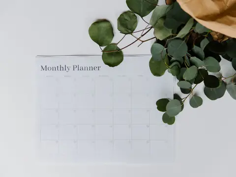A blank monthly planner page on a white desk with eucalyptus leaves beside it