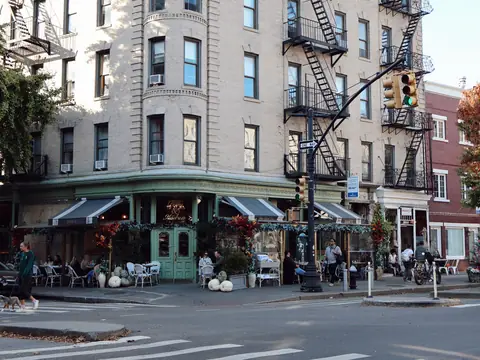 A New York street corner with a cafe under green awnings and tables on the pavement