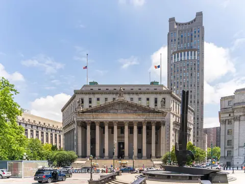 The New York County Courthouse in Manhattan: wide steps and a row of columns under a pediment, with flags at half height on the roof