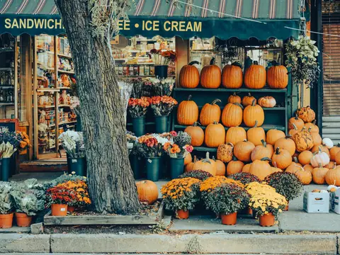 A New York corner shop with rows of pumpkins and potted flowers set out on the pavement under its awning