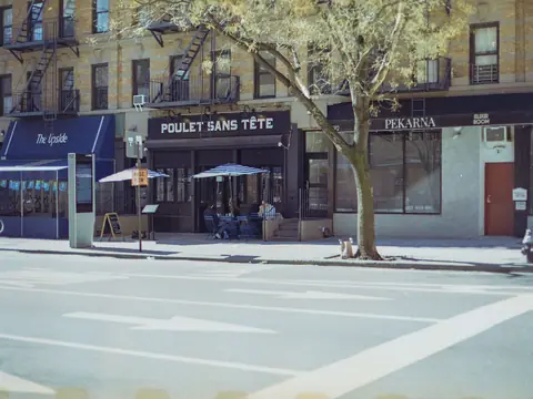 A New York avenue with restaurants under awnings, a tree and tables on the pavement