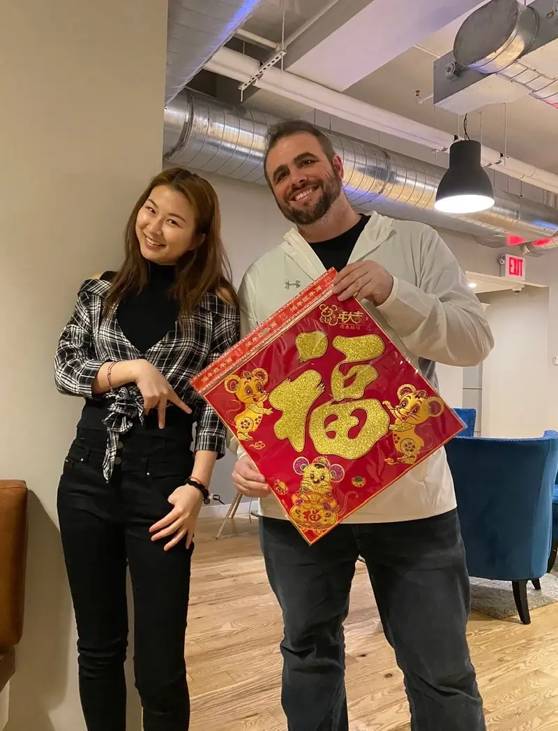 Christopher Maddaloni and a colleague smiling in an office common area, holding a red and gold Lunar New Year decoration between them
