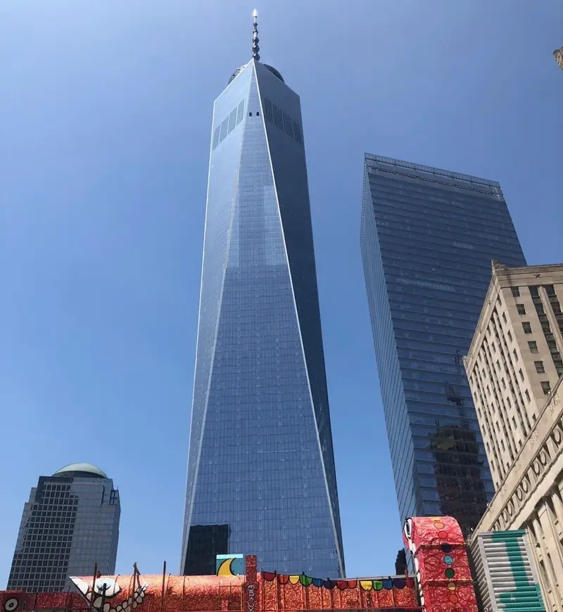 One World Trade Center seen from the street below against a clear blue sky, with neighbouring towers beside it