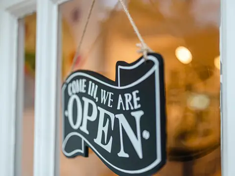 A black sign reading Come in, we are open hanging on string inside a shop's glass door