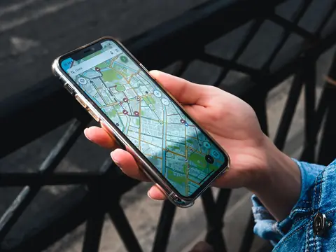 A hand holding a phone that shows a street map, beside an iron railing