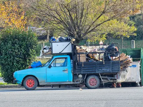 A small blue pickup truck piled high with cardboard and scrap, parked at a kerb