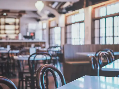 A restaurant dining room in daylight with bentwood chairs, white tables and tall windows