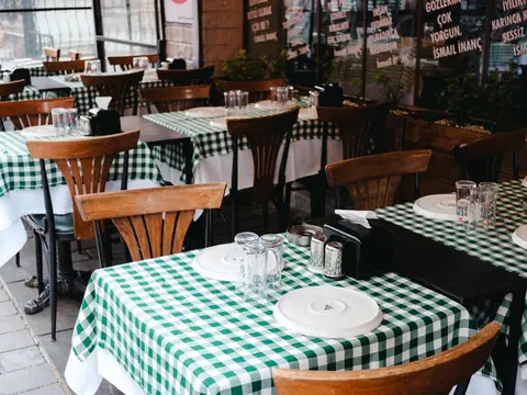 Restaurant tables with green check cloths and wooden chairs, set and empty