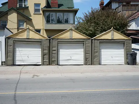 Three single garages with white doors side by side behind a house, seen from the street