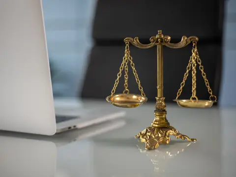 A small brass scale of justice standing on a white desk beside a laptop
