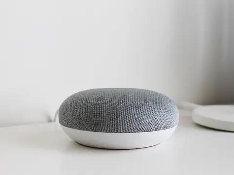 A small round grey smart speaker on a white shelf