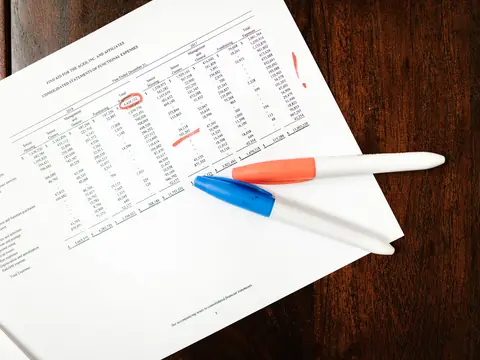 A printed table of figures with some circled in red, and two marker pens lying on it