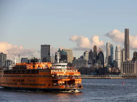 An orange Staten Island Ferry crossing New York Harbor with the city skyline behind it