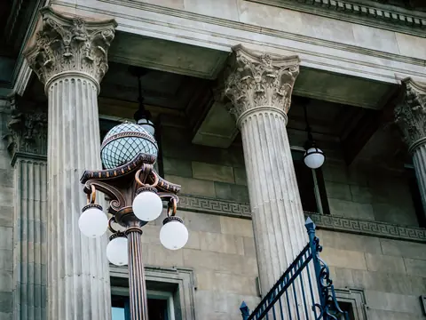 Tall stone columns of a public building with an old street lamp of round glass globes in front