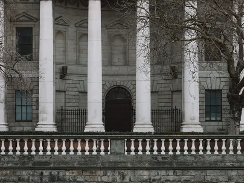 The stone front of a court building with tall white columns behind a balustrade