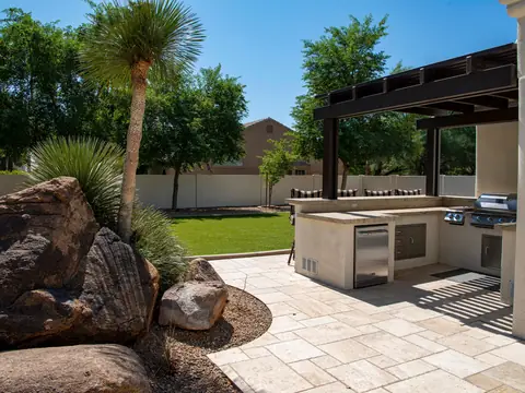 A stone patio with boulders, a palm and an outdoor kitchen under a pergola